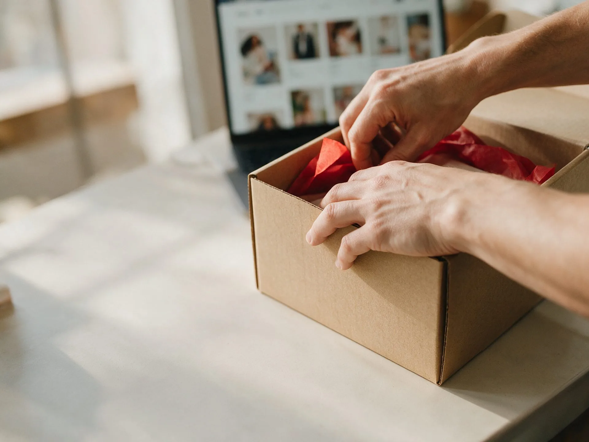 Manos empacando un pedido en línea junto a una laptop con la tienda abierta